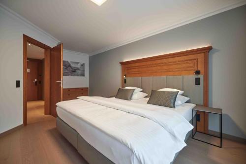 a bedroom with a large white bed with a wooden headboard at Hotel EDELWEISS Berchtesgaden Superior in Berchtesgaden