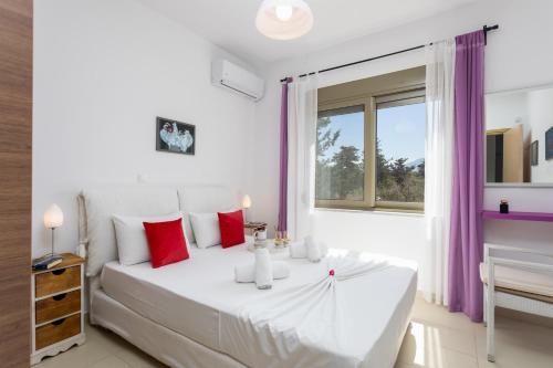 a white bedroom with a large white bed with red pillows at Villa Arda in Litsárdha