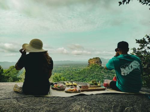 two people sitting on top of a rock with food on at Elephant safari Lodge sigiriya junction in Habarana