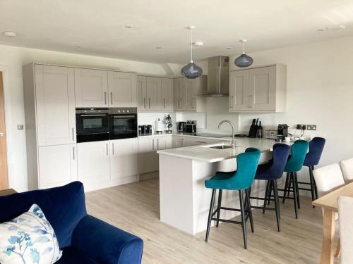 uma cozinha com armários brancos e bancos de bar azuis em Estuary View - Newly Built 3-Bed House em Conwy