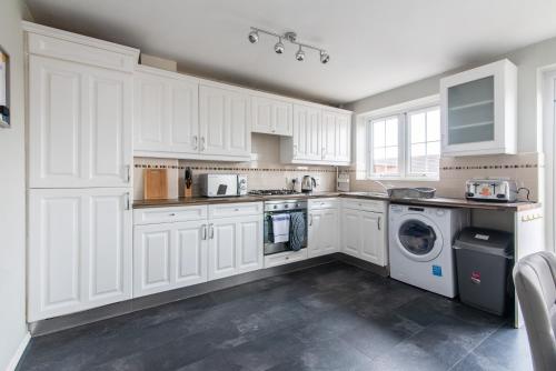 a kitchen with white cabinets and a washer and dryer at 3 Bed Gem in Pontefract for Easy Commutes to Leeds and Wakefield in Pontefract