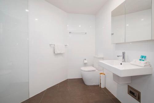 a white bathroom with a toilet and a sink at The Sandpiper - A Newy Beachfront Beauty in Newcastle