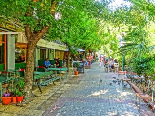 eine Straße mit Bänken, Tischen, Bäumen und Menschen in der Unterkunft Acropolis Luxury Apartments in Athen