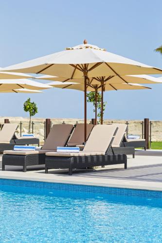 a group of lounge chairs and an umbrella next to a pool at Park Inn by Radisson Hotel and Residence Duqm in Duqm