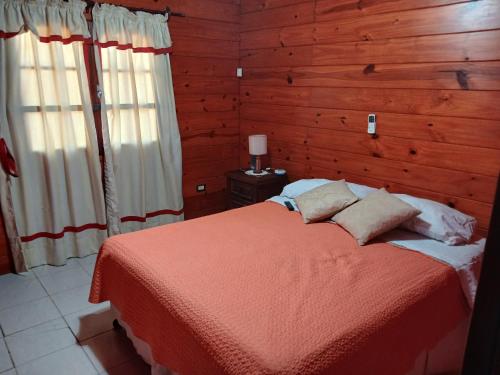a bedroom with a bed with red sheets and wooden walls at Cabaña/ Quincho San Ciro in Formosa
