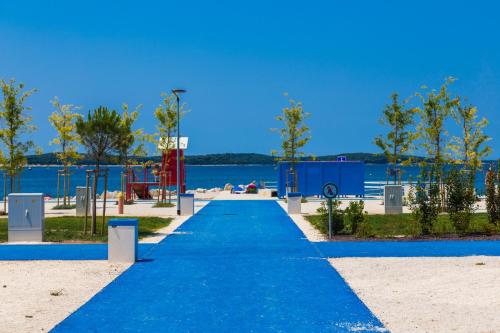 un chemin bleu menant à l'eau avec une aire de jeux dans l'établissement Apartman Vista Mare, à Pula