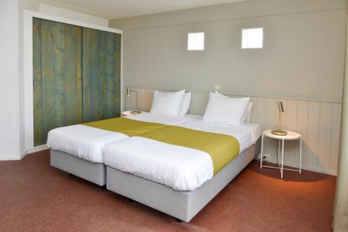 a bedroom with a large bed with a yellow blanket at Strandhotel Noordzee in De Koog