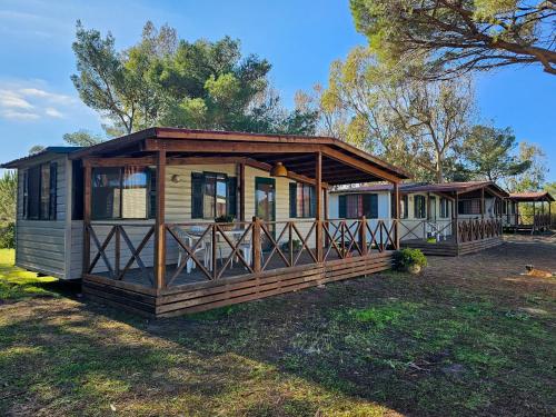a large wooden cabin with a porch on the grass at Camping Village S'Ena Arrubia in Arborea