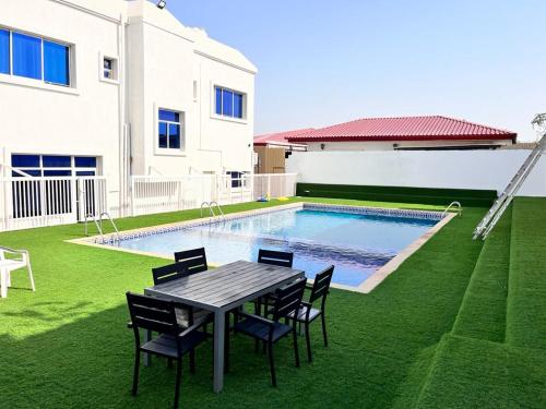 a backyard with a table and chairs and a swimming pool at 6 BEDROOMS FARM HOUSE VILLA FOR in Al Ḩamīdīyah