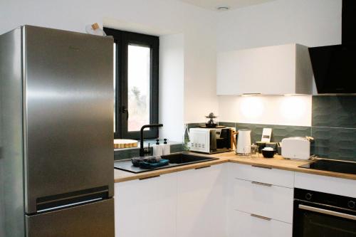 a kitchen with white cabinets and a stainless steel refrigerator at Les Blés Dorés et Les Graines de Lin, 2 gîtes à la Ferme avec moutons et piscine, à côté de Beaune in Corgengoux