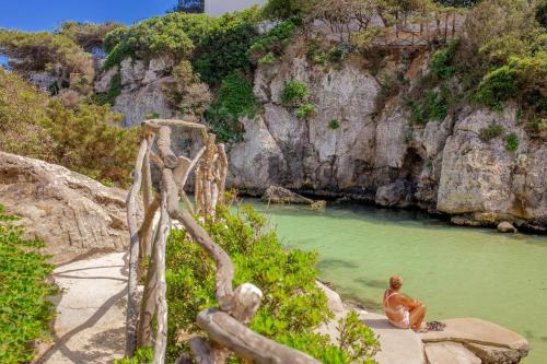 a man sitting on a rock in a body of water at Cala en Forcat in Cala en Forcat