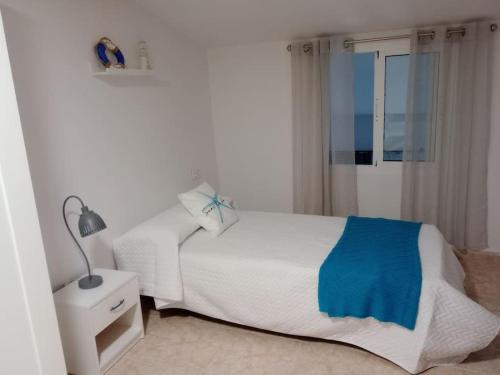 a white bedroom with a bed and a lamp and a window at Paraíso Azul in Aguadulce