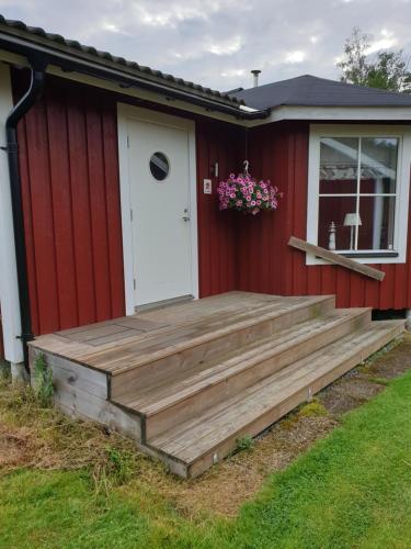 eine Holzterrasse an der Seite eines roten Hauses in der Unterkunft Semesterhus med spabad & bastu in Söderköping