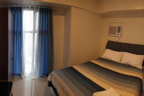 a bedroom with a bed and a window with blue curtains at Horizon 101, Condo with a pool & view in Cebu City