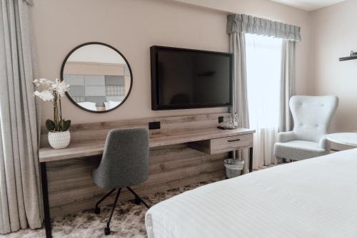een slaapkamer met een bureau, een televisie en een spiegel bij Cabarfeidh Hotel in Stornoway