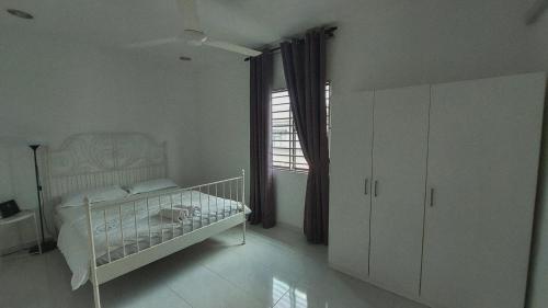 a white bedroom with a bed and a window at D'Sandra Homestay in Kulim