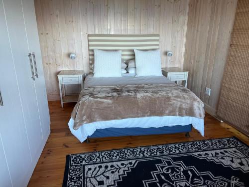 a bedroom with a large bed with two tables and a rug at Loerie Lodge in Keurboomstrand