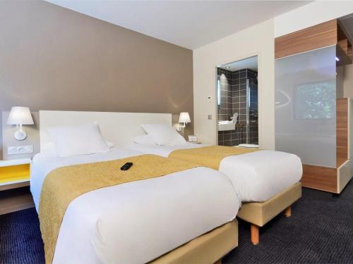 a hotel room with two beds and a bathroom at Kyriad Prestige Pau – Palais des Sports in Pau