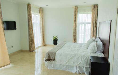 a bedroom with a bed with white sheets and windows at Divine Heights Apartments Lilongwe Area 43 in Lilongwe