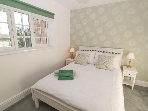a bedroom with a white bed with two windows at Hillside Hideaway in Wigton