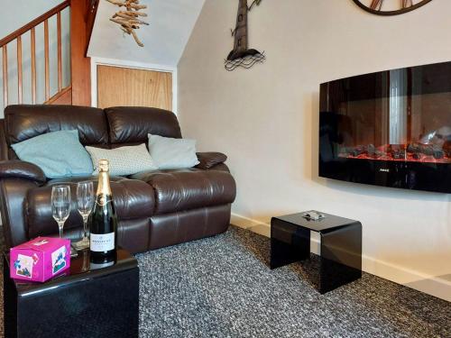 a living room with a brown leather couch and a bottle of wine at Swn Y Tonnau in Tywyn