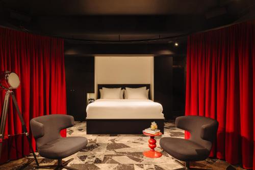 a bedroom with a bed with red curtains and two chairs at Leonardo Hotel Rotterdam Savoy in Rotterdam