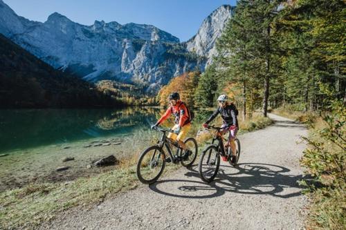 two people riding bikes on a path near a lake at Appartements Pension Elfi in Gosau