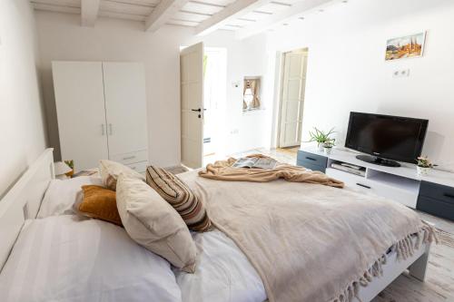 a white bedroom with a large bed and a flat screen tv at Malomvölgyi Vendégház in Balatonalmádi