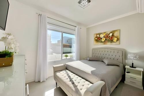 a white bedroom with a bed and a window at Casa 4 Suítes com piscina Fundos Lago-Ilhas Resort in Capão da Canoa
