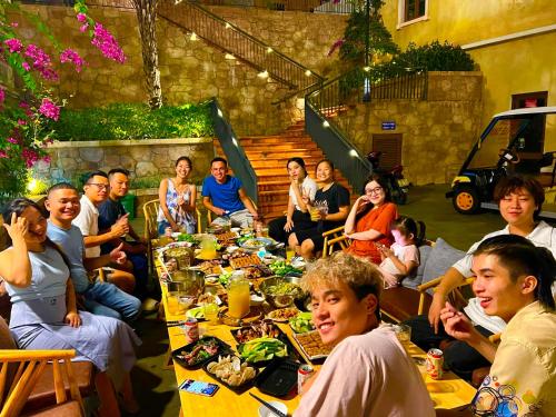 een groep mensen die rond een lange tafel zitten bij Sunset Hotel Phu Quoc - welcome to a mixing world of friends in Phu Quoc