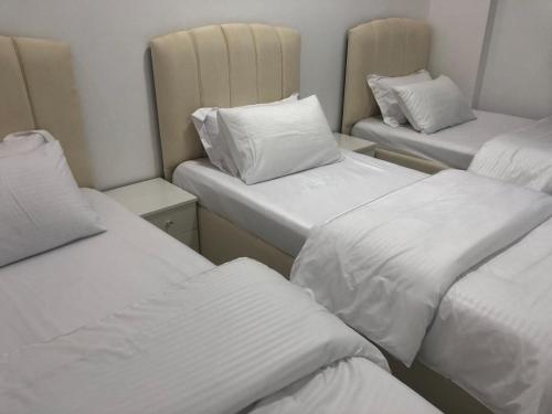 3 camas en una habitación con sábanas y almohadas blancas en ANTIKA HOTEL / انتيكا للشقق الفندقيه, en Firq
