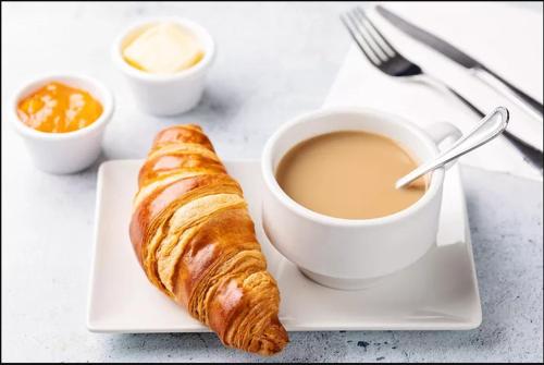 a plate with a cup of coffee and a croissant at Stay Inn Guest House in Islamabad