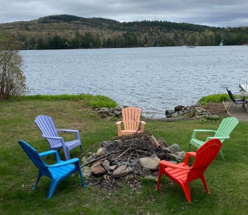 four colorful chairs around a fire pit by a lake at Spacious Lakefront Retreat w/Stunning Views in Hinesburg