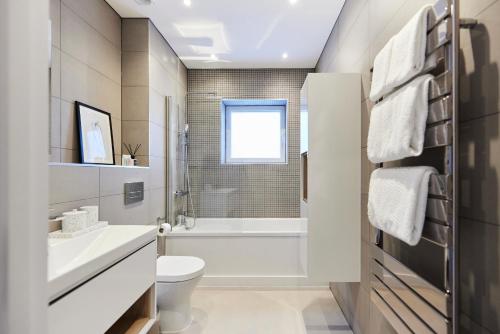 a white bathroom with a tub and a toilet and a sink at The Wembley Park Retreat - Modern 2BDR Flat with Balcony in London