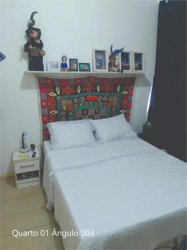 a bedroom with a white bed and a shelf with pictures at Quarto Carnaval 2024 Salvador in Salvador