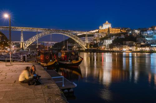 a woman sitting on a bench near the water with a bridge at Memoria Porto FLH Hotels in Porto
