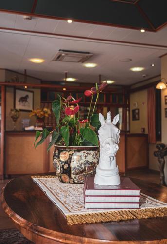 a vase sitting on a table with books and a plant at Hétkúti Wellness Hotel in Mór