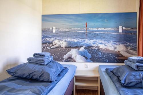 two beds in a room with a picture of the ocean at Chalet de Slufter Texel in De Cocksdorp