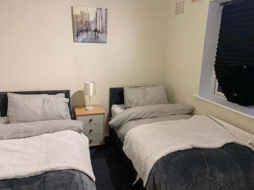 een slaapkamer met 2 bedden en een nachtkastje met een lamp bij Contractor & Family Friendly House Romford in Havering atte Bower