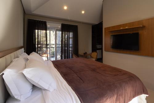 a bedroom with a bed with white pillows and a television at Vilinha típica - Suíte Onze Tuin - Entrada com senha - Somos hospedagem por temporada in Holambra