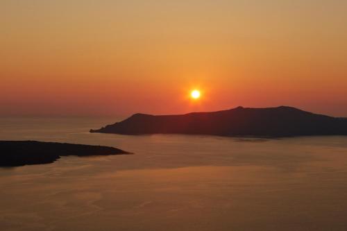 a sunset over the ocean with a mountain in the background at EDGE ON VOLCANO SUITES in Fira