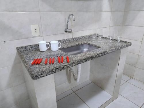 a bathroom counter with a sink and two mugs at Apartamento com vista para Montanha in Maricá