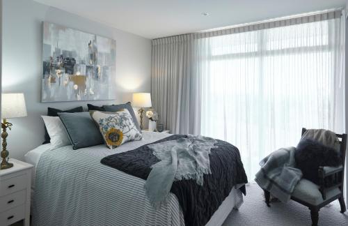 a bedroom with a bed and a chair and a window at Ocean + Country - Wainui Beach in Gisborne