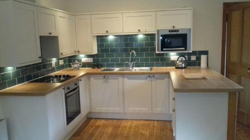 a kitchen with white cabinets and a sink and a microwave at Old School in Kingussie