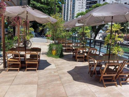 an outdoor patio with tables and chairs and umbrellas at Flat Pitangueira com Piscina-Capitânia Varan in Guarujá