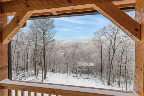 a window in a cabin looking out at a snow covered forest at Cozy Rustic Cabin in Sugar Mountain