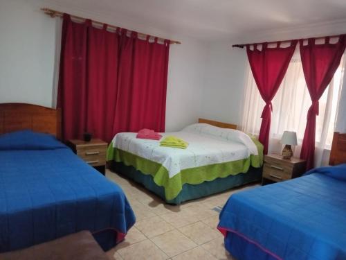 a bedroom with two beds and red curtains at Cabañas & Hostal Tojika in Hanga Roa