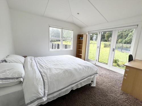 a bedroom with a bed with white sheets and windows at Ranfurly holiday home in Auckland
