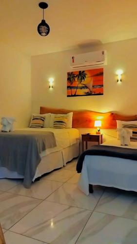 a bedroom with two beds and a table and a painting at Japaratinga Suites in Japaratinga