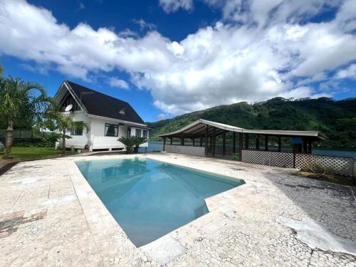a swimming pool in front of a house with a mountain at Taina - dans la baie de Faaroa in Taputapuapea